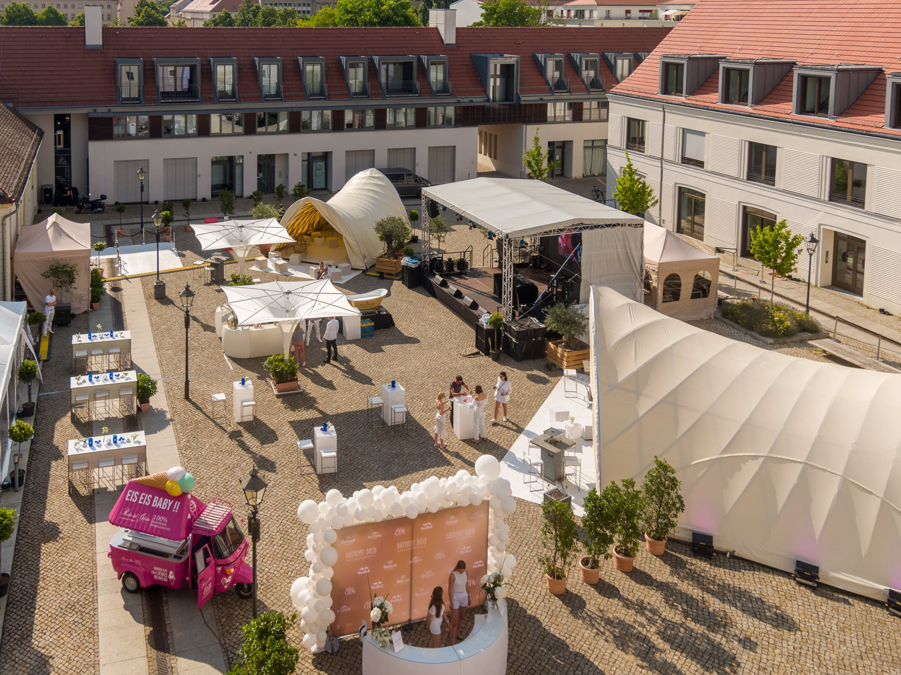 Der Innenhof von oben bei Tageslicht, Bühne, weiße Zelte und Sonnenschirme, Stehtische und der pinke Eiswagen auf dem Kopfsteinpflaster